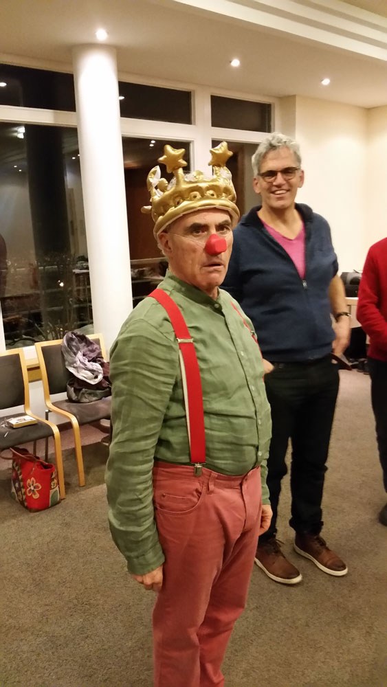 Clown mit goldener Krone und roter Nase neben einem Teilnehmer